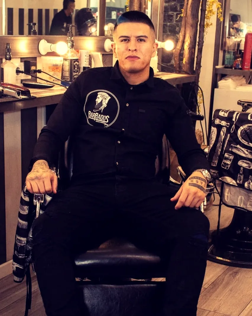 El barbero de La Perla sentado en el sillón, con el espejo de bombillas detrás