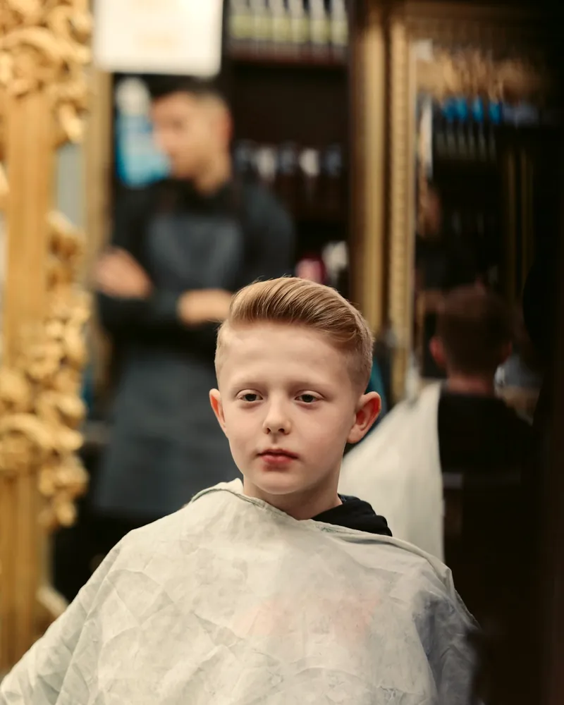 Niño con capa de barbería sentado en el sillón, recién peinado